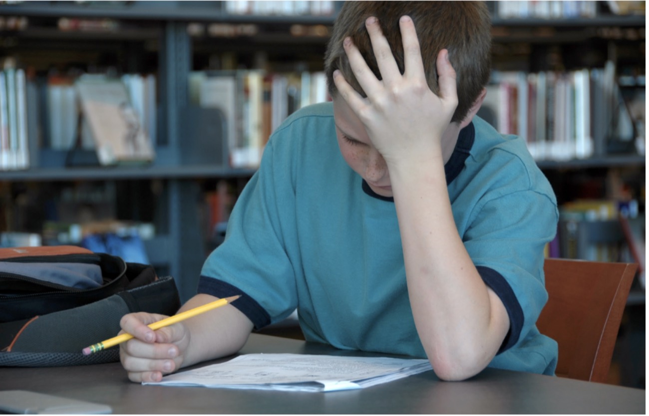 Adolescent découragé, la tête dans la main devant ses devoirs